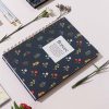 La libreta "Florece" de UO* en un entorno decorativo con flores naturales y bolígrafos, ideal para acompañar momentos de planificación o escritura creativa.