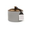 Elegante vela de cera de soja con fragancia de vetiver y cardamomo, presentada en un recipiente de cerámica verde suave con tapa de metal en tono cobre. Ideal para crear un ambiente acogedor y sofisticado en cualquier espacio.