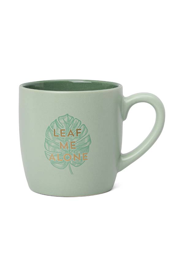 Taza de cerámica en tono verde claro con interior verde oscuro. Presenta un diseño con una hoja de monstera y el mensaje en relieve "LEAF ME ALONE", jugando con un juego de palabras en inglés. Ideal para los amantes de la naturaleza y los mensajes divertidos.