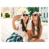 Dos chicas con gafas de sol al aire libre usando la cámara para capturar una selfie.