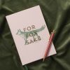 Cuaderno de tapa dura en tono beige con la frase "For Fox Sake" acompañada de una ilustración de zorro en verde y dorado. Incluye marcapáginas de cinta verde y páginas diseñadas para notas y planificación.