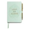 Un elegante cuaderno en color verde menta con la frase "Leaf Me Alone" en letras doradas sobre una ilustración de hoja tropical. Incluye un bolígrafo dorado sujeto con una banda elástica lateral y un marcador de página en cinta de raso.